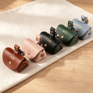 May include: Five small leather pouches in brown, light pink, black, dark green, and light blue. Each pouch features a gold-tone snap button closure, a metal clip, and gold embossed initials reading AM, CF, GM, WE, and PM respectively.