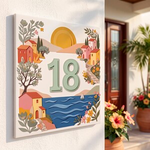 Könnte beinhalten: Ein quadratisches Hausnummernschild mit der Zahl 18 in Salbeigrün. Das Design zeigt eine mediterrane Küstenszene mit bunten Häusern, einer gelben Sonne, einem blauen Meer mit einem Segelboot sowie floralen Elementen in Rosa und Orange.
