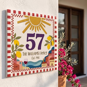 Peut inclure: Une plaque de maison carrée en céramique avec une bordure à carreaux rouges et blancs. Le centre affiche le nombre 57 en violet, le texte THE WILLIAMS FAMILY Est. 1981, un soleil jaune, des branches de citronnier, un verre de vin et un village côtier.