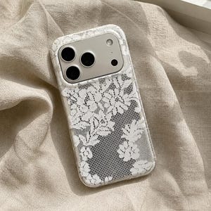 以下が含まれることがあります： 白い花柄のレース模様が施された透明なスマートフォンケース。ケースは角が丸い長方形で、上部にはカメラレンズ用の切り抜きがあり、3つの黒い円としてレンズが見えています。