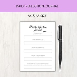 May include: A white daily reflection journal page with black text and lines, featuring sections for date, quote of the day, gratitude, self-care, smiles, and future outlook. A black ballpoint pen is positioned vertically to the right of the paper.