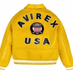 May include: A bright yellow leather jacket featuring the black text AVIREX and USA on the back. A circular patch in the centre displays the text ALL AMERICANS ESTABLISHED 1975 with a graphic of the American flag. The jacket has a ribbed hem.