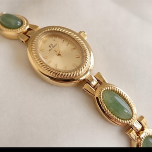 Può includere: Un orologio da polso color oro con quadrante ovale color champagne recante la scritta BS Bee Sister. Il cinturino è composto da maglie metalliche color oro alternate a pietre verdi ovali e lisce con un bordo dalla trama a corda.