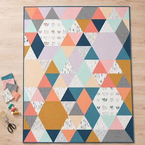 Op de afbeelding: Een rechthoekige quilt met een geometrisch patroon van driehoeken en zeshoeken in tinten koraal, taling, mosterdgeel, lavendel en grijs. Het ontwerp bevat effen en bedrukte stoffen met illustraties van vossen en bomen.