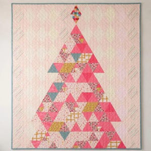 May include: A rectangular quilt featuring a central triangular tree motif composed of various pink, yellow, and teal geometric fabric patches. The background is a pale pink diamond-stitched pattern with striped vertical borders and a teal edge.