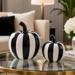 May include: Two decorative pumpkins featuring a glossy finish with alternating vertical black and white stripes. Each pumpkin has a smooth, rounded body and a curved black stem extending from the top, creating a high-contrast, monochromatic look.