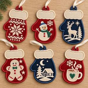 May include: Six embroidered mitten-shaped ornaments with cream-colored hanging ribbons. Designs include a snowflake, a snowman, a deer, a gingerbread person, a winter cabin scene, and a mug with a candy cane, all featuring cream-colored cuffs.