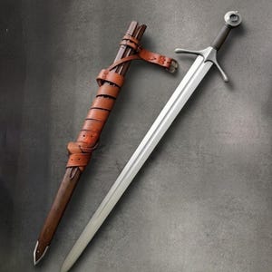 May include: A steel sword with a straight, double-edged blade, a cross-guard, and a circular pommel. Beside it lies a brown wooden scabbard wrapped in brown leather straps with a metal tip at the bottom and a buckle attached to the side.