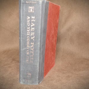 May include: A hardcover book titled "Harry Potter and the Goblet of Fire." The spine is gray with gold lettering and a small emblem. The book's edge is red. The book is slightly angled.