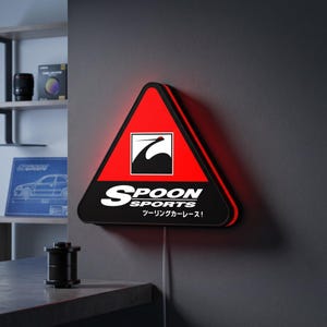 May include: A triangular LED wall sign featuring a red top section with a black crane logo and a black bottom section with the white text SPOON SPORTS and Japanese characters. The sign emits a red glow from its edges and includes a power cord.