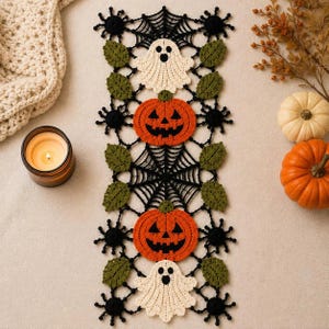 May include: A rectangular crochet table runner featuring a black spiderweb pattern interspersed with two white ghost motifs, two orange jack-o'-lanterns, and several green leaves. The design includes small black spider accents.