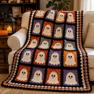 May include: A handmade crochet blanket featuring a repeating pattern of white ghost motifs with black eyes and mouths. Each ghost is centered within a square frame of alternating orange, purple, and black yarn, finished with a scalloped border.