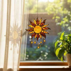 Peut inclure: Un capteur de soleil en vitrail en forme de soleil avec un disque central jaune entouré de pointes rayonnantes orange et rouges. L'objet comporte plusieurs petites gouttes en verre suspendues aux bords inférieurs de la structure.