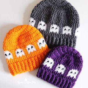 Puede incluir: Tres gorros de ganchillo en naranja, gris oscuro y morado, cada uno con una banda de motivos de fantasmas blancos con ojos negros. El texto "Repeat Crafter Me" es visible en blanco abajo a la izquierda. Los gorros tienen un borde acanalado.
