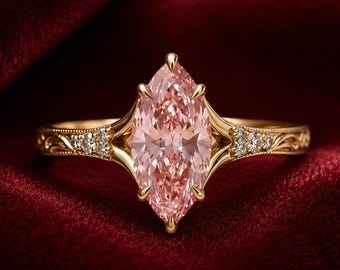 May include: A gold ring featuring a large marquise-cut peach-colored gemstone held by six prongs. The band is crafted with intricate engraved scrollwork details and is accented by three small round clear stones on each side of the center gem.