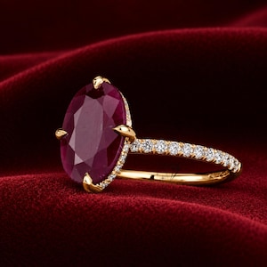 Può includere: Un anello in oro con un grande rubino rosso intenso taglio ovale come pietra centrale, fissato da quattro griffe. La fascia è realizzata in oro giallo ed è impreziosita da una fila di piccoli diamanti rotondi e chiari incastonati a pavé.