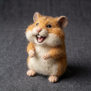 May include: A needle-felted hamster figurine with a fuzzy texture, featuring a golden-brown back, a cream-colored belly, and small ears. The hamster has a wide, open-mouthed expression showing two white front teeth, black eyes, and a pink nose.