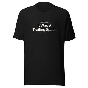 May include: A black short-sleeved crew neck t-shirt featuring white text centered on the chest. The text reads DEBUGGING in a small font above the larger, bolded phrase It Was A Trailing Space. The garment is a solid black color throughout.