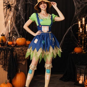 May include: A scarecrow costume featuring a light green short-sleeve top, a blue denim-style overall dress with plaid patches, and a pointed tan hat. The outfit includes tan knee-high socks with plaid patches and frayed straw-like trim details.