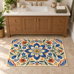 Può includere: Un tappetino da bagno rettangolare caratterizzato da un motivo floreale simmetrico con un grande fiore centrale blu e giallo, circondato da fiori arancioni, boccioli blu e foglie verdi su sfondo crema, con accenti decorativi blu agli angoli.