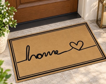 Op de afbeelding: Een rechthoekige, lichtbruine deurmat met een zwarte dubbele lijnrand. Het woord home is geschreven in een doorlopend zwart cursief lettertype dat aan de rechterkant uitloopt in een hartvorm op het matoppervlak.