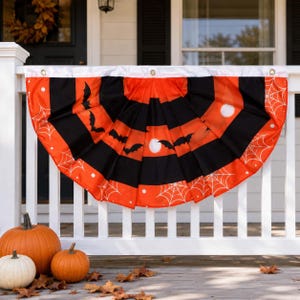 Könnte beinhalten: Eine halbkreisförmige, gefaltete Stoffgirlande im Halloween-Design mit abwechselnden schwarzen und orangefarbenen Streifen, schwarzen Fledermaussilhouetten, weißen Spinnennetzmustern und weißen Punkten, versehen mit einem weißen Rand und Metallösen.