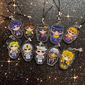 May include: A collection of nine clear acrylic charms featuring chibi-style anime characters with colourful outfits and hair. Each charm is attached to a black cord strap with a silver-toned metal clasp, showcasing various distinct character designs.