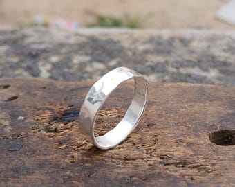 May include: A silver-colored ring with a hammered, textured surface. The band has a polished, reflective finish that catches the light, showing irregular indentations across its outer circumference, creating a distinct, non-uniform appearance.