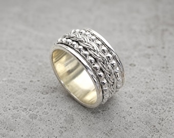 May include: A wide silver spinner ring featuring a central braided band flanked by two rows of small, textured metallic beads. The ring has a polished, reflective interior surface and a multi-layered design with a bright, metallic silver finish.