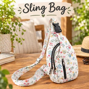 May include: A white sling bag featuring a colorful floral pattern with small red, blue, and yellow flowers. The bag has a quilted texture, a black plastic buckle on the strap, and two black zippered pockets on the front. The text "Sling Bag" is visible.