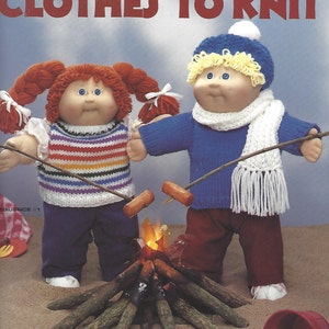 Könnte beinhalten: Eine 40,6 cm große Soft-Skulptur-Puppe mit gestrickter Kleidung, mit dem Text "CLOTHES TO KNIT". Die Puppe trägt einen blauen Hut, Schal und Pullover. Die andere Puppe trägt einen gestreiften Pullover und eine lila Hose.