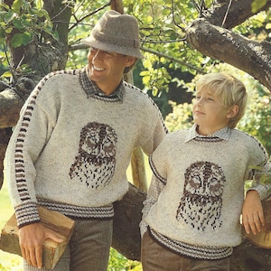 Puede incluir: Dos jerséis beige a juego con diseños de búhos. Uno tiene mangas largas con rayas marrones, el otro es sin mangas. Un hombre y un niño llevan los jerséis sobre camisas con cuello, al aire libre.