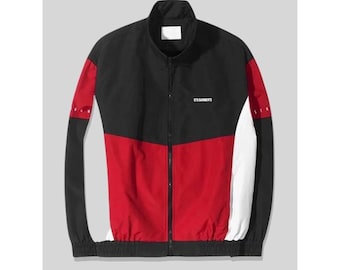 Puede incluir: Una chaqueta deportiva de bloques de color negro, rojo y blanco con cuello alto, cremallera frontal completa y puños y dobladillo elásticos. En el pecho se muestra el texto en blanco ETD GARMENTS y detalles de texto en las mangas.