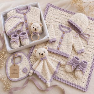 Puede incluir: Un set de regalo de ganchillo con artículos de hilo color crema y lavanda: dos cárdigans con botones de madera, dos gorritos con lazos, dos pares de patucos, un babero con etiqueta Heirloom Newborn Gift Set Organic Cotton, un sonajero de oso y un doudou.