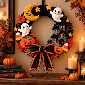 Könnte beinhalten: Ein gehäkelter Halloween-Kranz mit schwarzer Basis, verziert mit einem gelben Halbmond, zwei weißen Geistern, zwei orangefarbenen Kürbissen, einem grauen Spukhaus, gelben Sternen, Zuckermais und roten Ahornblättern, abgerundet durch eine große schwarz-orange Schleife.