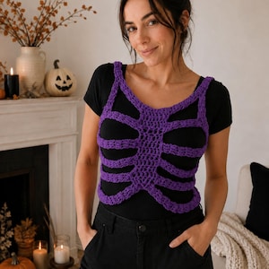 Peut inclure: Un haut en crochet violet en forme de cage thoracique porté sur un t-shirt noir à manches courtes et un pantalon noir. La pièce en crochet présente un motif de colonne vertébrale centrale avec des structures horizontales en forme de côtes.