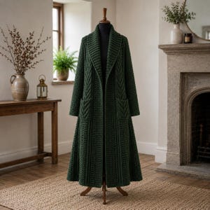May include: A long, dark forest green open-front cardigan featuring a thick shawl collar, long sleeves, and two front patch pockets. The garment is crafted with a textured, vertical cable knit pattern throughout, extending to a floor-length hemline.