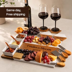 May include: A rectangular wooden and white serving board engraved with "Emilia & Steven January 12, 2025", three white square bowls with wooden spoons, a wine bottle, two wine glasses, hexagonal coasters, and a set of four cheese knives.