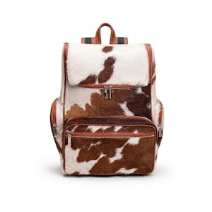 May include: A backpack featuring a brown and white cowhide pattern with a textured fur finish. The bag includes a top handle, adjustable shoulder straps, a large main compartment with a zipper closure, and a smaller front pocket with a zipper.