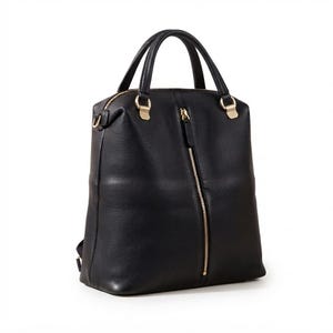 May include: A black backpack with a textured surface, featuring two top handles and a vertical gold-toned zipper running down the center of the front panel. The bag includes gold-toned hardware attachments for the handles and side straps.