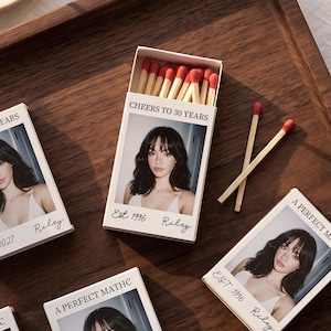 May include: Several rectangular matchboxes featuring a custom photo of a person with dark hair, the text "CHEERS TO 30 YEARS" or "A PERFECT MATCH", "Est. 1996", and the name "Riley". The boxes contain wooden matches with red tips.