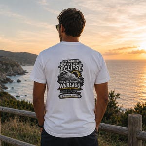 Peut inclure: Un t-shirt blanc avec un motif au dos portant le texte "YO TAMBIÉN ESTUVE EN EL ECLIPSE Y ESTABA NUBLADO ASTURIAS 12-08-2026 NO ES EXCUSA, ES DESTINO" accompagné d'une illustration d'un nuage grincheux et d'une éclipse solaire.