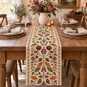 May include: A long rectangular table runner featuring a cream-colored fabric with a repeating botanical pattern of brown acorns, green oak leaves, and clusters of red berries, centered on a wooden dining table with place settings and a vase.