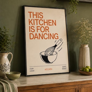 以下が含まれることがあります： クリーム色の背景にオレンジ色の文字で「THIS KITCHEN IS FOR DANCING」と書かれ、その下にボウルに入った泡立て器の黒い線画が描かれた長方形の額入りウォールアートプリント。ボウルの下には「COOK」「LAUGH」「KITCHEN」「DANCE」「REPEAT」という単語が配置されています。