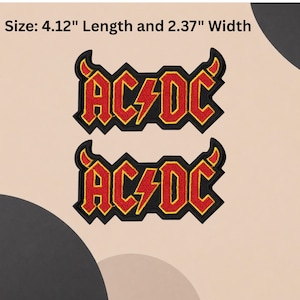 Op de afbeelding: Twee geborduurde patches met het AC/DC-logo in rood met gele omlijningen en zwarte randen, inclusief kleine rode duivelshoorntjes op de letters A en C. De tekst vermeldt een lengte van 10,46 cm en een breedte van 6,02 cm.