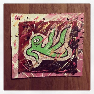 May include: Green and black abstract painting on a textured canvas with pink, white, and gold accents. The painting features a stylized creature with large eyes and multiple arms.