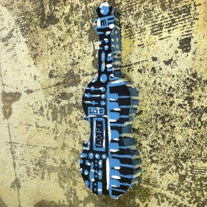 May include: A blue and black painted wooden sculpture of a violin with a keyboard design. The sculpture is painted with a variety of geometric shapes and patterns.