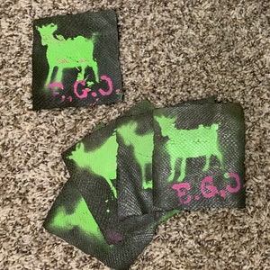 May include: Four black fabric coasters with a green goat silhouette and pink "E.G.O." text. The coasters have a textured surface.