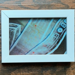 May include: A close-up of a white framed photo of a blue and white patterned fabric with red and orange spots.