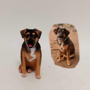 May include: A hand-painted dog figurine featuring a black and tan coat with a white chest marking, sitting in a forward-facing position. Beside it is a photograph of a real dog with similar coloring, sitting on a dirt path with its mouth open.